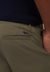 Shorts vert olive en tissu léger avec une taille élastique, ornés d'un petit teckel brodé sur la poche arrière.