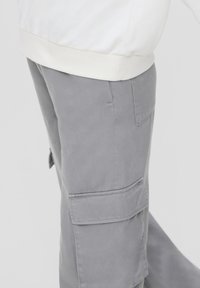 Grijze cargo pants met meerdere zijzakken, een soepele textuur en een relaxte fit, gecombineerd met een witte sweatshirt om de taille.