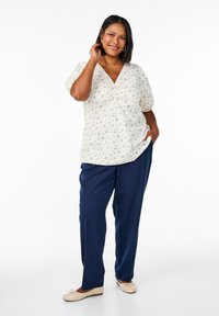 White floral blouse with a V-neck and short puff sleeves, paired with navy trousers and light beige flat shoes.