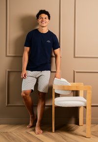 Marinblå bomulls t-shirt med korta ärmar, ihopparad med ljusgrå mönstrade shorts. En trästol med en texturerad vit sittdyna står i närheten.