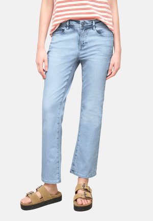 Personne portant un jean droit bleu clair, un haut sans manches rayé et des sandales compensées beiges avec des brides à double boucle.