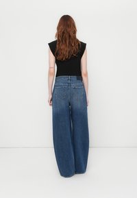 Vide benbukser i blå denim med høj talje, to baglommer og en gradvis lysningseffekt på bunden. Kombineret med en sort top.