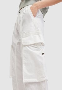 Witte cargobroek met een ontspannen pasvorm, voorzien van grote zijzakken, trekkoorddetails en een gestructureerde stofafwerking.