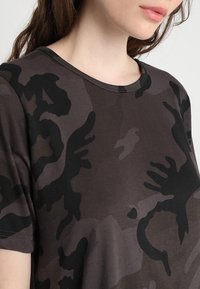 Dark brown t-shirt with a camouflage pattern, featuring a round neckline and short sleeves. Soft fabric with varied shades of brown and black.