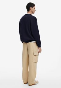Sudadera oversize azul marino con cuello redondo combinada con pantalones cargo beige que presentan múltiples bolsillos y un detalle cosido en el lateral.