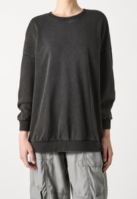 Sudadera gris oscura con cuello redondo, puños y bajo con fruncidos. Fabricada en un tejido suave, cuenta con un corte relajado y un diseño minimalista.