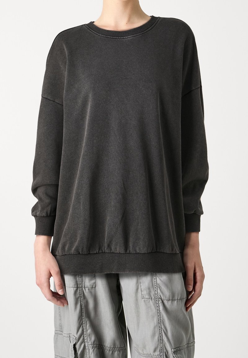 Sudadera gris oscura con cuello redondo, puños y bajo con fruncidos. Fabricada en un tejido suave, cuenta con un corte relajado y un diseño minimalista.