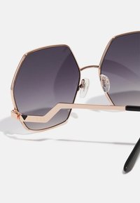Ochelari de soare hexagonali cu lentile gradient violet, ramă metalică rose gold, suporturi pentru nas transparente și tempuri negre. Prezintă logo-ul brandului.