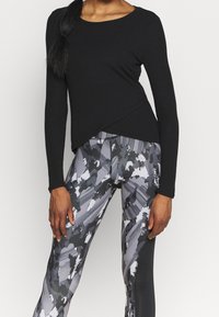 Czarna bluzka z długim rękawem o pochylonym dole, zestawiona z dopasowanymi legginsami w szaro-czarny abstrakcyjny wzór z teksturowanym wykończeniem.