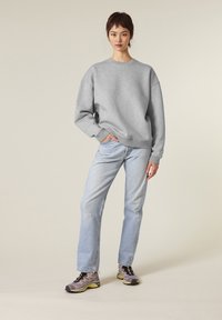 Felpa grigia oversize con polsini a costine, jeans azzurri a gamba dritta e scarpe sportive grigie con accenti gialli.