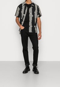 Camicia a maniche corte con motivo a righe ondulate in bianco e nero, abbinata a pantaloni neri e stivali neri con lacci. Texture piatta e liscia.