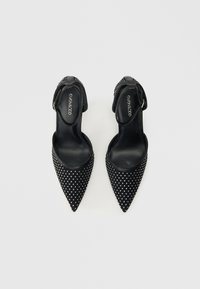 Zapatos de tacón alto negros con puntas afiladas, adornados con tachuelas plateadas. Con una correa en el tobillo con una pequeña hebilla. Textura suave.