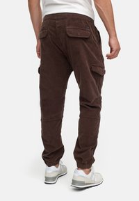 Pantalones cargo marrones hechos de una tela suave, con bolsillos laterales, puños elásticos y un corte relajado. Combinados con zapatillas deportivas ligeras.