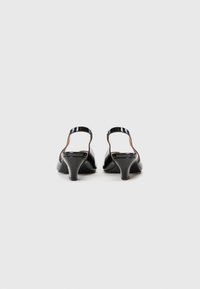 Chaussures en cuir verni noir avec un design à bout fermé et un petit talon. Elles présentent une sangle mince autour de la cheville et une texture lisse.