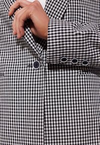 Czarny i biały żakiet w kratę w stylu gingham z wyciętym kołnierzem, zapięciem na jeden guzik oraz detalem trzech guzików na mankietach. Teksturowana tkanina.