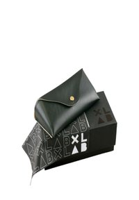 Borsetta in pelle nera con un bottone dorato in cima, poggiata su una scatola nera con un motivo a logo bianco ripetuto e un panno per la pulizia in tessuto nero.