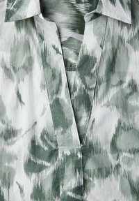 Lätt, grön och vit mönstrad tyg med krage och V-formad öppning; har en texturerad, abstrakt design.