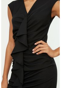 Robe noire avec un décolleté en V profond, des manches courtes, et un design froncé présentant des volants asymétriques sur le devant, texture du tissu lisse.