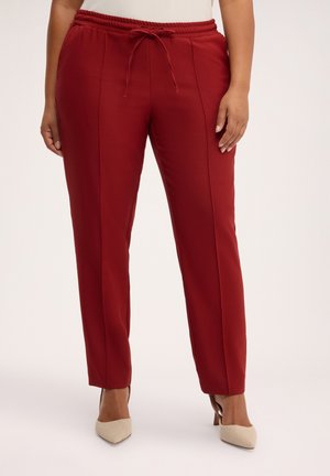Mujer con pantalones hechos a medida de color rojo intenso con cintura elástica y cordón, combinados con tacones beige de punta afilada.