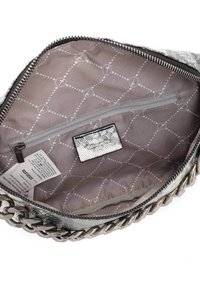 Vnitřek metalicky stříbrné kabelky s šedým vzorovaným podšívkou, obsahující kapsu na zip a štítek, obklopený zipem ve stylu řetězu.