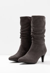 Botas de tobillo de ante gris con un diseño arrugado, puntera en punta y tacón de 5 cm; cuenta con una cremallera lateral para facilitar su uso.
