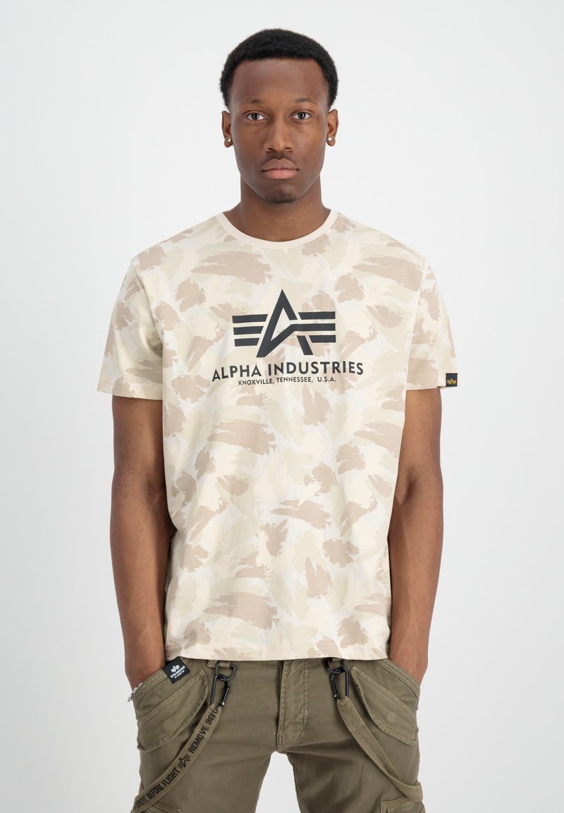 Beige camouflage T-shirt med korta ärmar, har svart "Alpha Industries"-logga på bröstet, slätt tyg, rund halsringning.