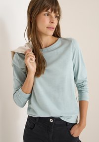 Helles blau gestreiftones Langarmhemd mit rundem Ausschnitt, kombiniert mit dunklen Hosen. Der Stoff ist weich und hat eine glatte Textur.
