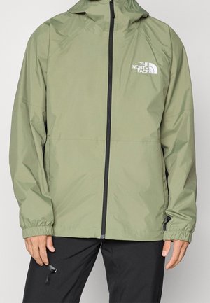 Mężczyzna w oliwkowo-zielonej kurtce z kapturem North Face z przednim zamkiem błyskawicznym oraz czarnych spodniach.