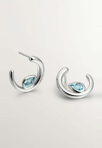 Pendientes de aro de plata con un diseño ondulado y suave, y un acento de gema azul en forma de pera. El metal pulido crea una superficie reflectante.