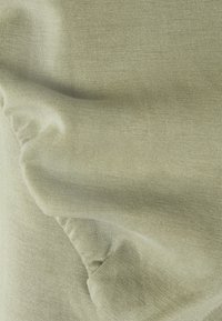 Gros plan sur un tissu tricoté vert sauge clair et doux avec une texture côtelée fine et de subtiles plis et rides.