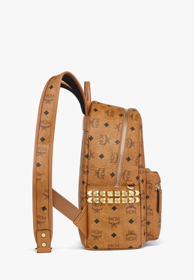 Sac à dos en cuir tan avec logos embossés et motifs en diamant. Présente des clous dorés sur la poche avant, une fermeture éclair et des bretelles ajustables.