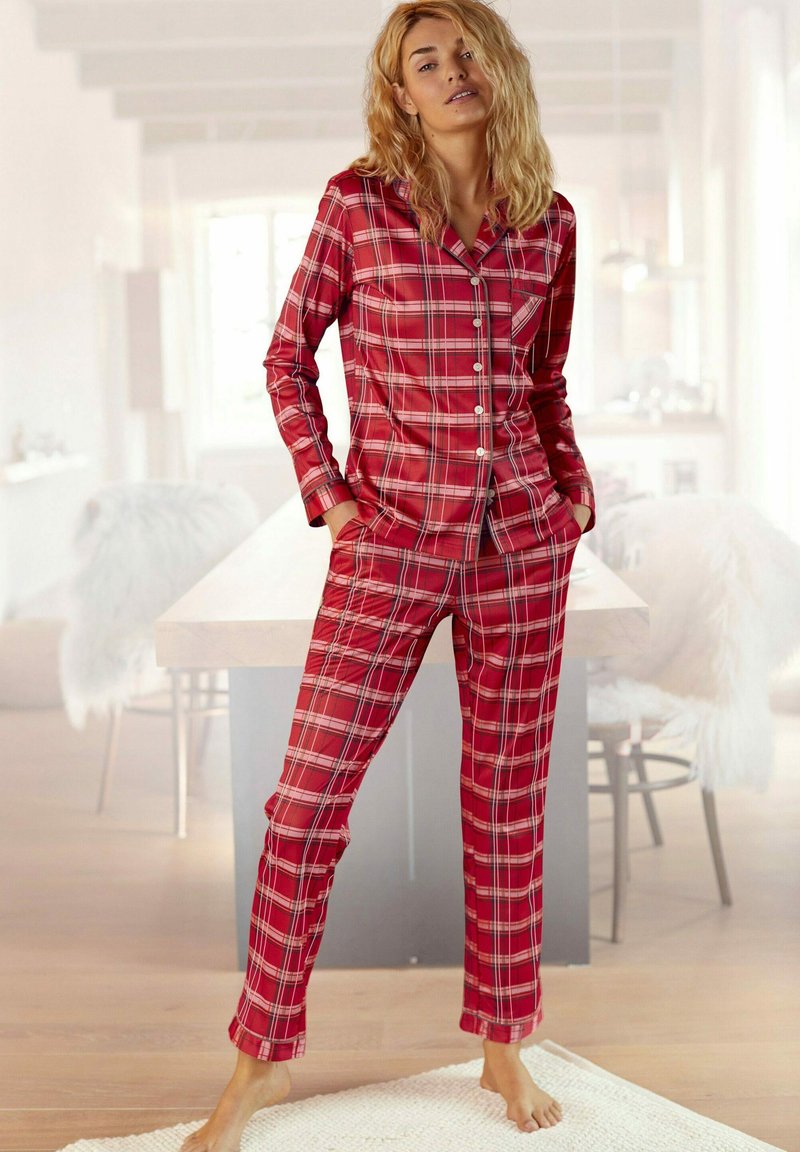 Red plaid pajamas feature a button-up shirt with long sleeves and matching pants. The fabric appears soft with traditional check patterns.