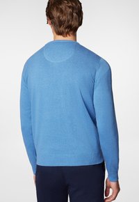 Niebieski lekki sweter z długimi rękawami, okrągłym dekoltem i prążkowanym wykończeniem. Ma gładką fakturę oraz subtelne detaliczne przeszycie na plecach.