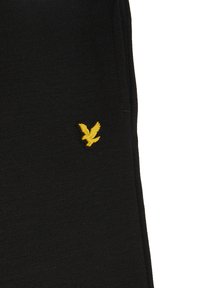 Sort bomuldsstof med en struktureret overflade, prydet med et lille gult fuglelogo på venstre side nær lommen.