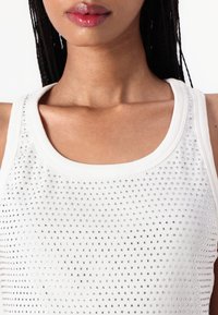 Weißes Tanktop mit strukturiertem Muster und kleinen, gleichmäßig verteilten metallischen Akzenten. Gerippter Ausschnitt und Armöffnungen, ärmelloses Design.