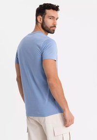 Světle modré tričko s krátkým rukávem vyrobené z jemné látky, s klasickým kulatým výstřihem a uvolněným střihem, nošeno s béžovými cargo kalhotami.