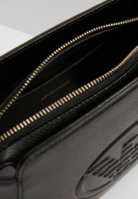 Clutch in pelle nera con finitura testurizzata, zip dorata e logo impresso. L'interno è foderato con un materiale liscio, che rivela il nome del marchio.