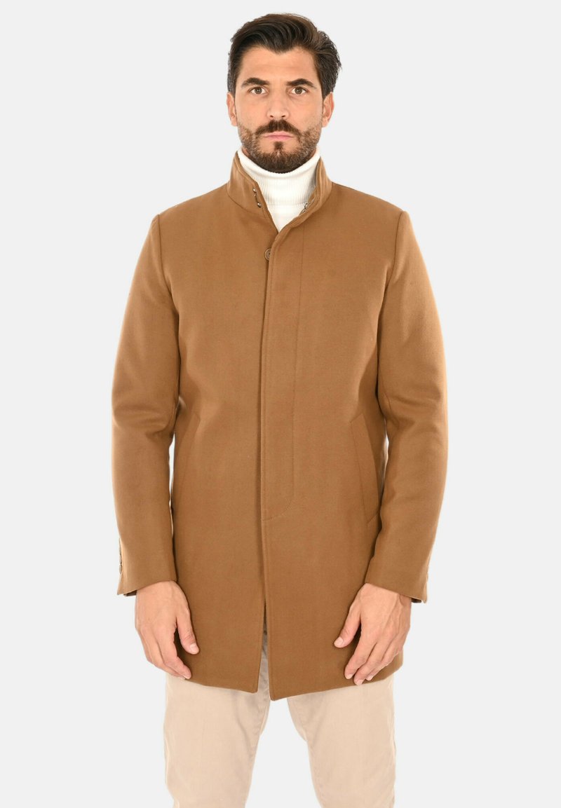 Cappotto di lana marrone con collo alto, caratterizzato da un taglio dritto, tasche laterali e una texture liscia. Indossato sopra un dolcevita bianco.