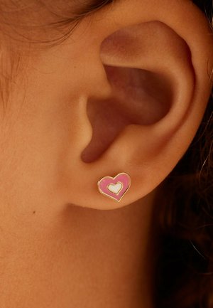 Boucle d'oreille en forme de cœur rose avec un plus petit cœur blanc incrusté, monté sur un métal doré. Surface en émail lisse, fixé à une oreille percée.