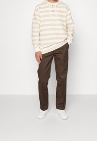 Sweat à capuche rayé crème et beige avec une poche avant et trois boutons. Associé à un pantalon marron foncé et des baskets blanches.