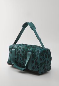 Grønn leopardmønstret duffelbag med svarte aksenter, stoffmateriale, doble håndtak og justerbar skulderrem. Sirkulære ender og glidelås.