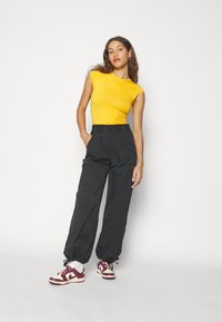 Gul tajts topp, svarta cargobyxor med sidofickor, och vinröda och vita sneakers. Kompletterande outfit mot en helt vit bakgrund.