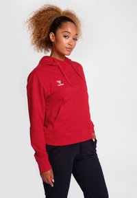 Roter Kapuzenpullover mit einer Vorderasche und verstellbarem Kordelzug. Mit einem Logo auf der Brust, aus weichem, elastischem Stoff gefertigt.