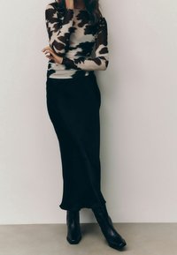 Long-sleeve top features a black and beige tie-dye pattern; paired with a sleek black midi skirt and black ankle boots with a pointed toe.