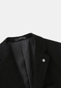 Blazer en velours côtelé noir avec revers cranté, deux poches avant et un petit badge rond sur le côté gauche. Doublure intérieure lisse.