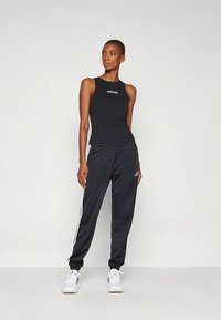 Svart ermeløs topp med hvit Adidas-logo, kombinert med svarte joggebukser med hvite side-striper og hvite treningssko.