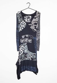 Långärmad, flerfärgad tunika med varierande grafiska mönster, djup halsringning och asymmetrisk fåll, främst i mörkblå och grå nyanser.