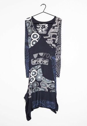 Túnica de manga larga y multicolor con variados patrones gráficos, escote profundo y dobladillo asimétrico, principalmente en tonos azul oscuro y gris.