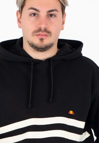 Felpa nera con cappuccio, con strisce orizzontali bianche che attraversano il petto e un piccolo logo multicolore sul lato sinistro. Tessuto morbido.