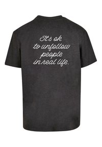 Sort bomulds t-shirt med korte ærmer og en afslappet pasform. Teksten på ryggen lyder: "Det er okay at følge folk fra i det virkelige liv" i hvid håndskrift.
